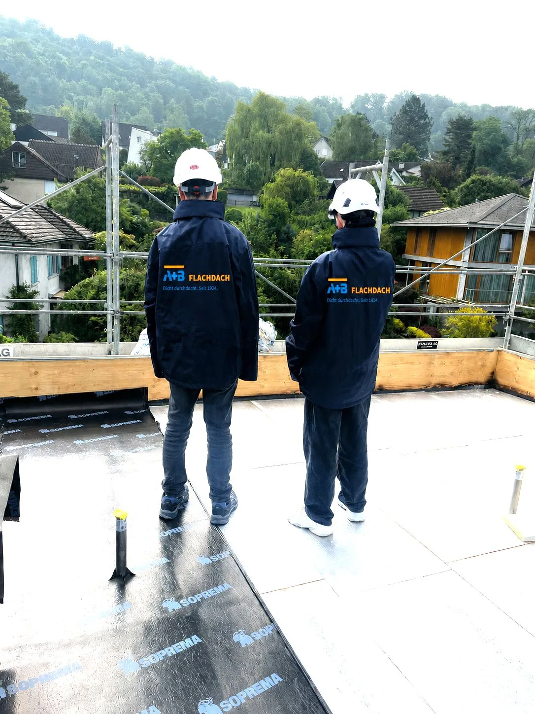 Zwei Lernende von A+B Flachdach auf dem Flachdach mit Blick über die Umgebung